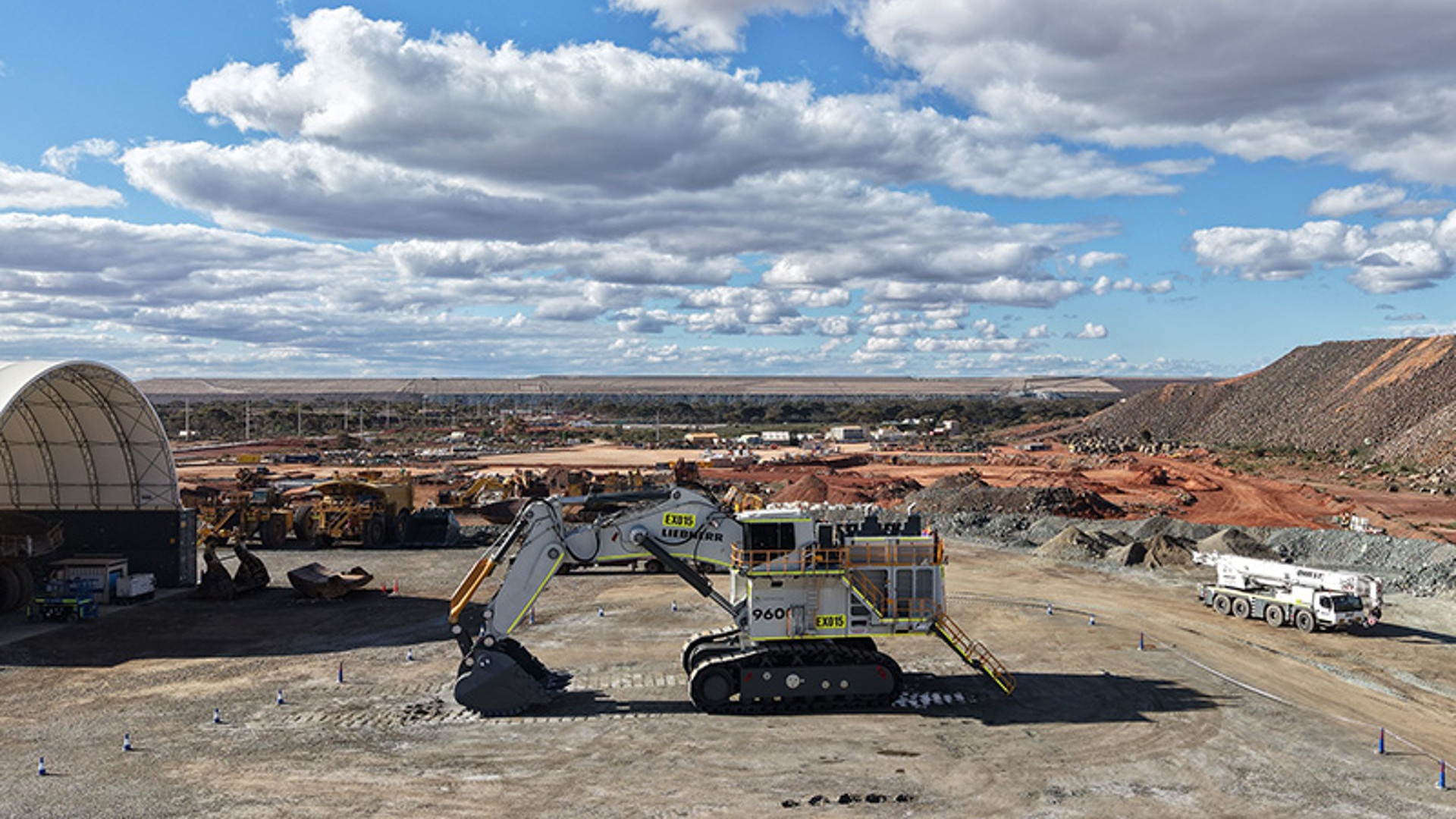 Liebherr R 9600 mining excavator standing on a hardstand at the Super Pit gold mine in Western Australia, with the existing haul truck fleet and a waste dump behind it