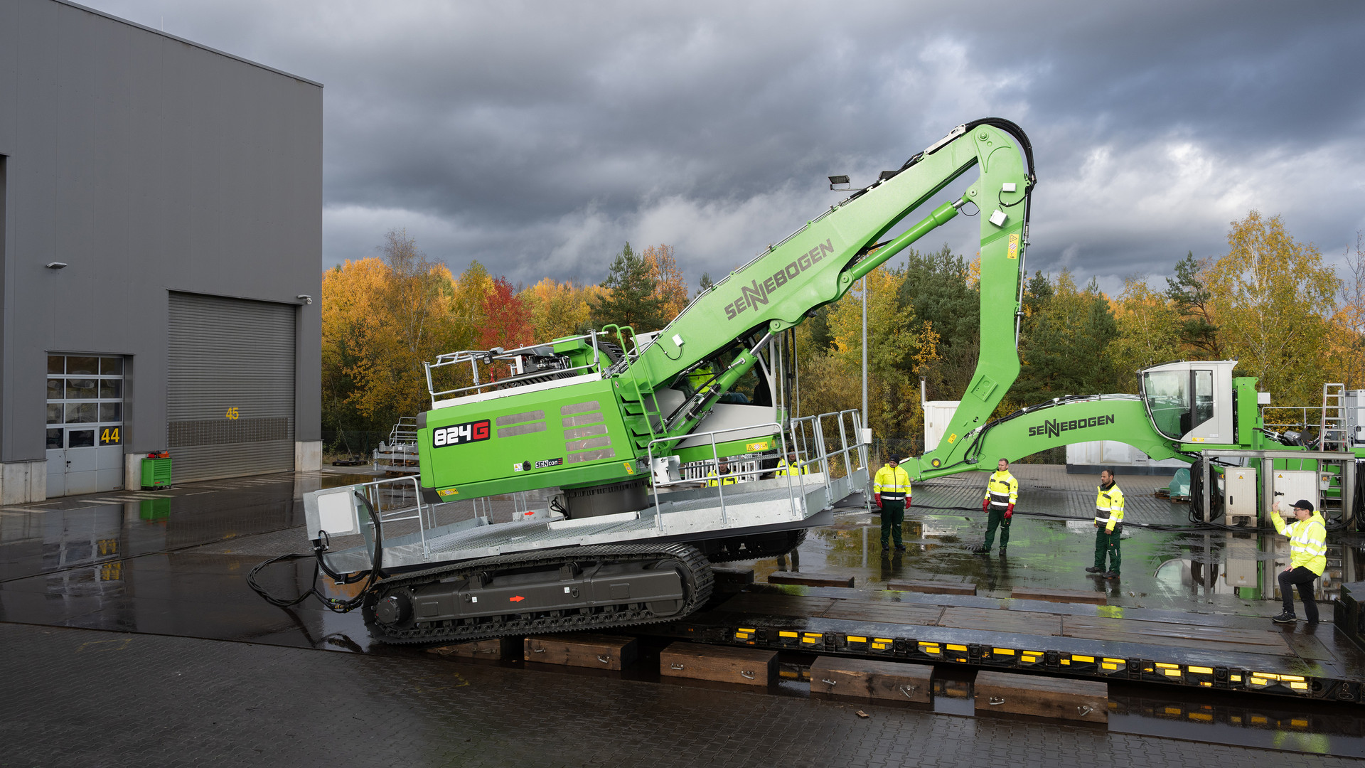 SENNEBOGEN 824 G Electro material handler tracking onto a low-loader at the SENNEBOGEN plant, boom folded, 824 G badge and SENcon decal visible, service walkways fitted